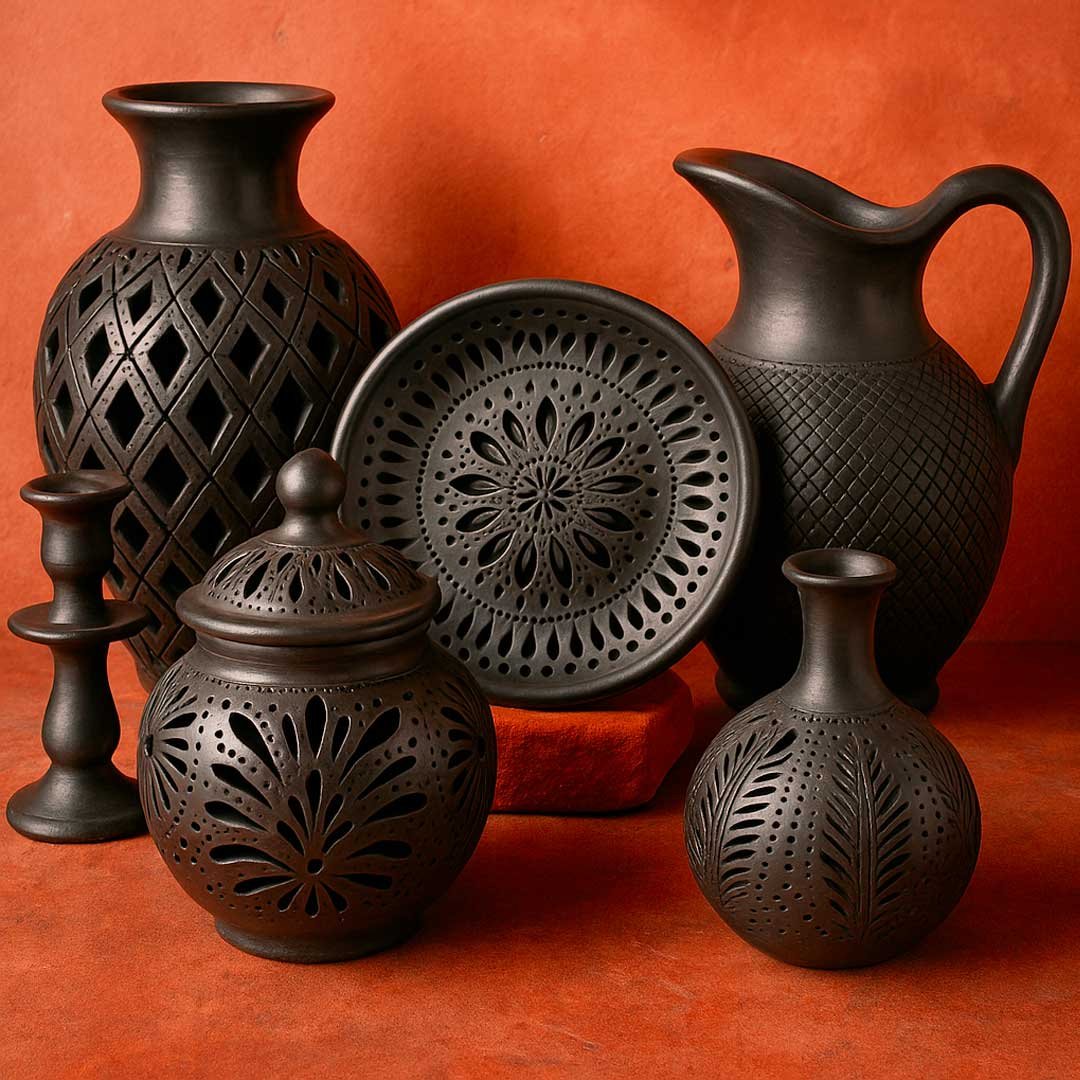 A collection of six traditional Oaxacan barro negro pottery pieces displayed against a terracotta background, including a lidded jar, a geometric vase, a candlestick holder, a decorative plate, a small vase, and a large pitcher, all with intricate carvings and a matte black finish.