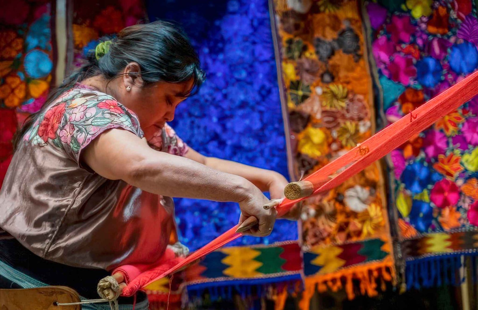"Maya woman weaving traditional textiles with a backstrap loom, surrounded by vibrant colors, featured on our Mexico Cultural Tour."